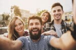 Four young happy people posing together for a selfie outside.